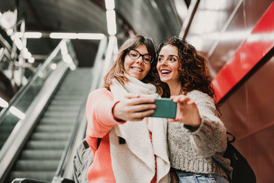 Happy young woman using mobile phone while standing on steps