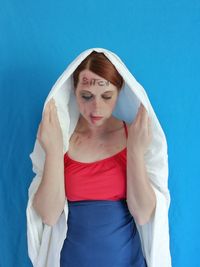 Thoughtful woman with wounds standing against blue wall