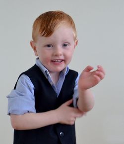 Close-up portrait of smiling boy standing against white wall