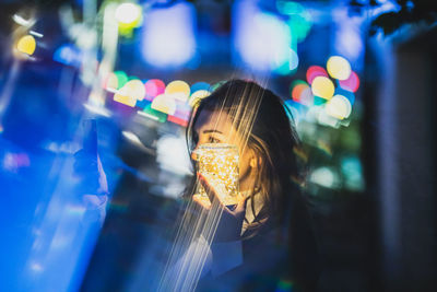 Digital composite image of woman with illuminated lighting equipment using smart phone while standing outdoors at night