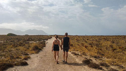 Rear view of couple walking on dirt road against sky