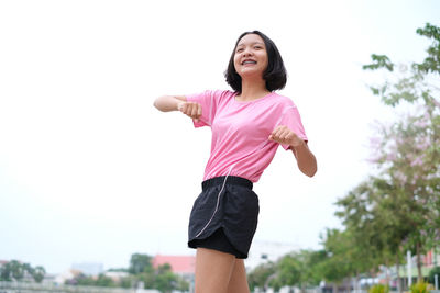 Low angle view of smiling teenage girl looking away while standing against clear sky