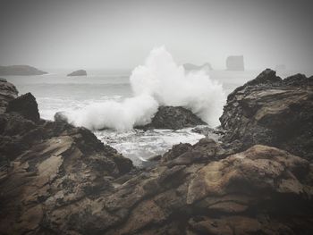 Waves breaking on rocks against sky