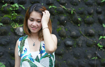 Close-up of young woman with hand in hair standing against wall