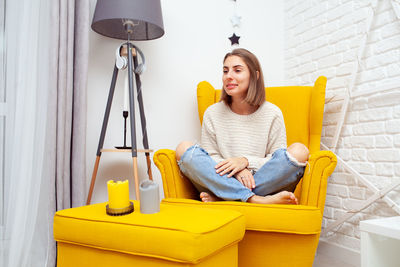 Smiling woman sitting on yellow armchair at home