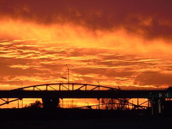 Silhouette bridge over city against sky at sunset