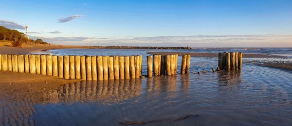 Wooden posts on beach against sky during sunset