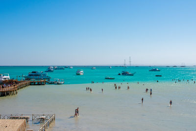 People at beach against clear blue sky