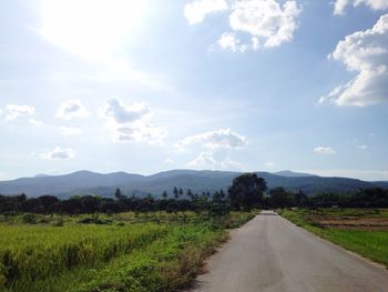 Empty road amidst field against sky