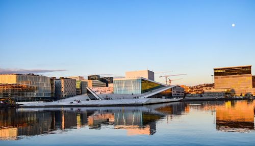 Reflection of buildings in city against clear blue sky