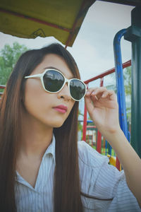 Close-up portrait of young woman wearing sunglasses against sky