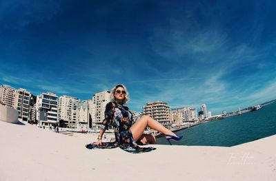 Young woman sitting by sea against sky