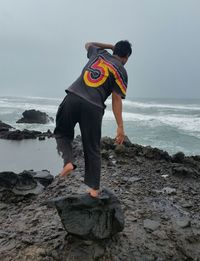 Man standing on rock at beach against sky