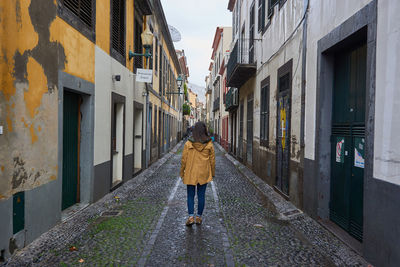 Rear view of woman standing on footpath amidst buildings