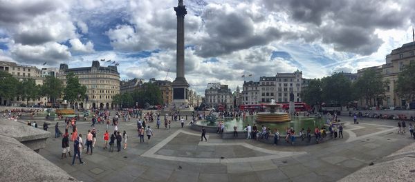 Panoramic view of people at town square against cloudy sky