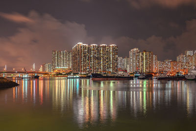 Illuminated modern buildings by sea against sky at night