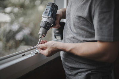 Caucasian man installs fittings for a window frame with a drill.