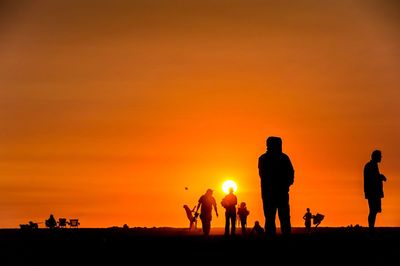 Silhouette people against orange sky during sunset