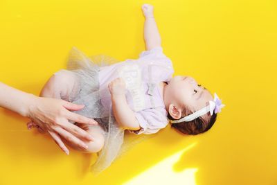 Cropped hand of woman holding baby girl lying on yellow table