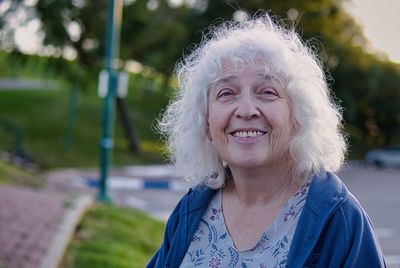Attractive grey-haired curly senior woman smiling while looking at the camera.