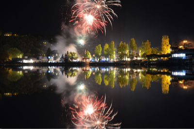 Reflection of firework display and trees in lake at night