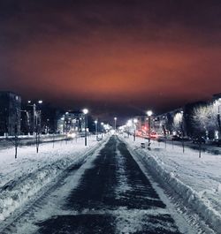 Road by snow covered city against sky at night