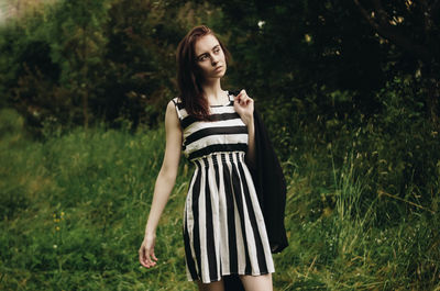 Beautiful young woman standing on grass against trees