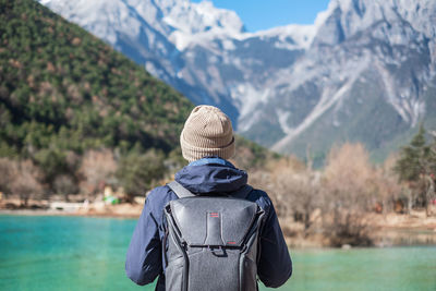 Rear view of woman standing by lake against mountains