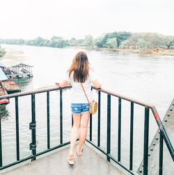 Rear view of woman standing by railing against sky