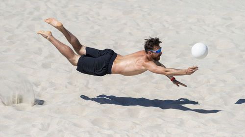 Shirtless man playing volleyball at beach