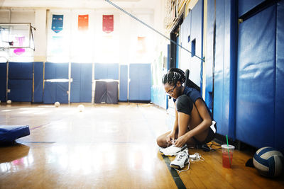 Teenage girl sitting on floor and tying shoelace in court