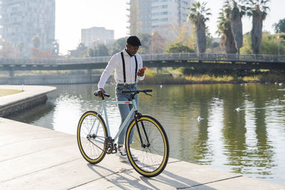 Man using mobile phone by bicycle on footpath in city