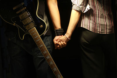 Midsection of man with guitar holding hand of woman over black background