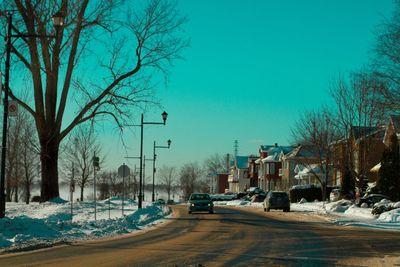 Snow covered road by trees against clear sky