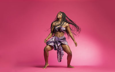 Young woman dancing against pink background
