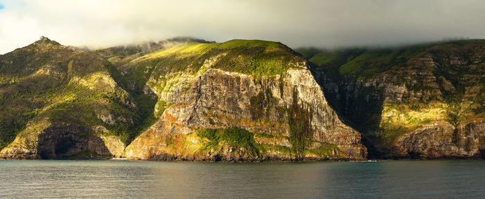 Scenic view of sea by mountain against sky