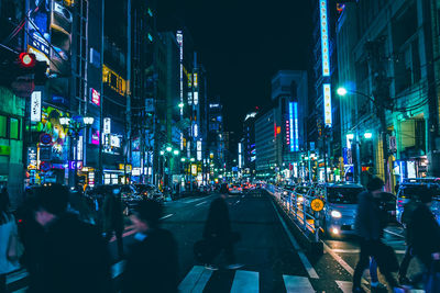 People on illuminated street amidst buildings at night