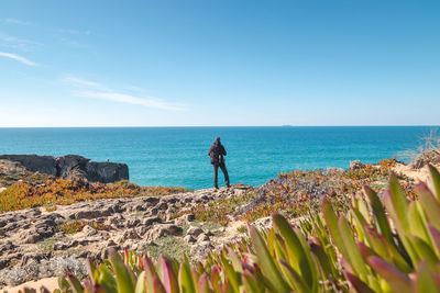 Rear view of woman standing on beach against blue sky