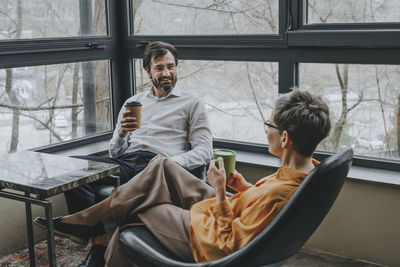 Smiling businessman having coffee break and discussing with colleague in office