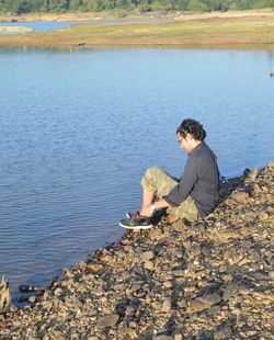 Side view of man sitting on rock by lake