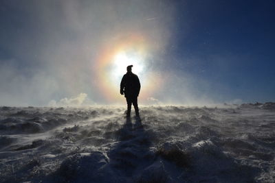 Rear view of silhouette man standing on shore against sky