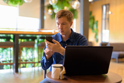 Young woman using phone while sitting on table