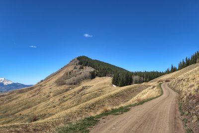 Dirt road by mountain against blue sky