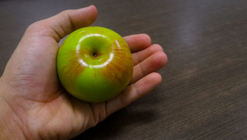 Cropped image of hand holding apple on table