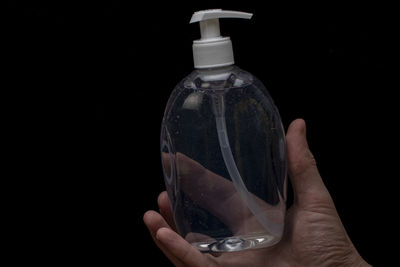 Close-up of hand holding glass bottle against black background