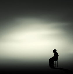 Silhouette man sitting on seat against sky