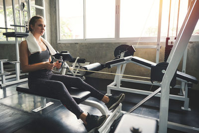 Young woman lowering weight of fitness machine and working out in the fitness gym