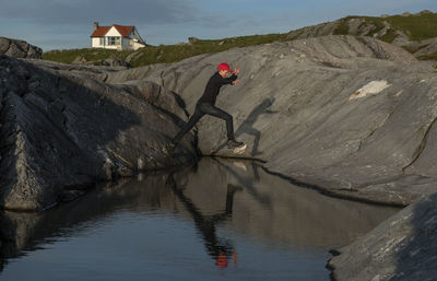 Full length of man jumping over water on rock against sky