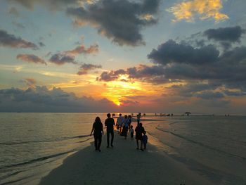 People walking at beach against sky during sunset