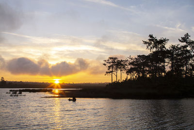 Silhouette trees by lake against sky during sunset